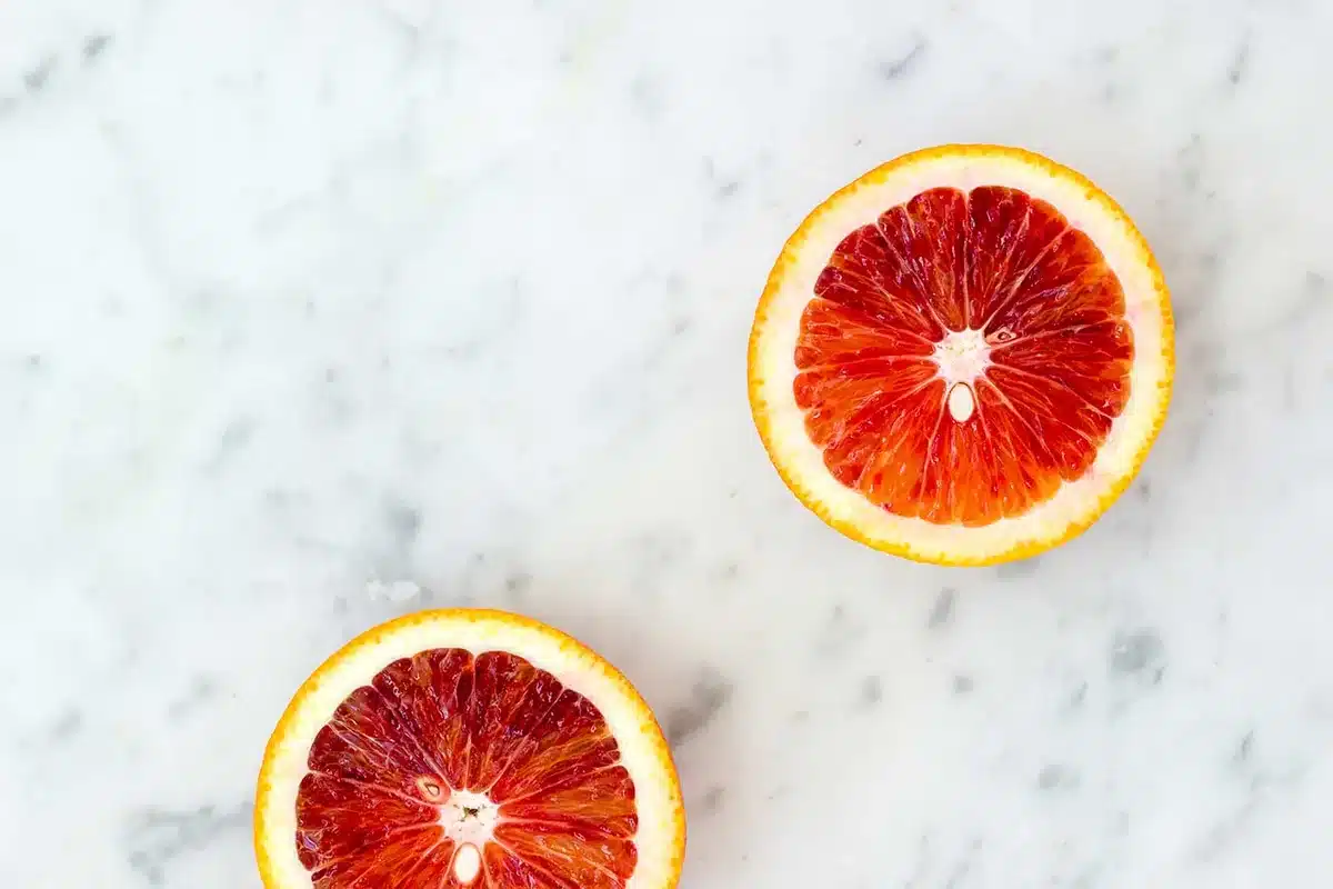 Two blood orange halves cut side up on a pale marble counter