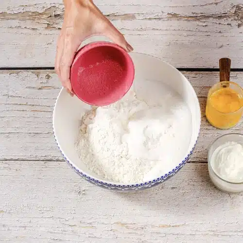 Clear soda poured from a pink cup into a bowl of dry baking mix