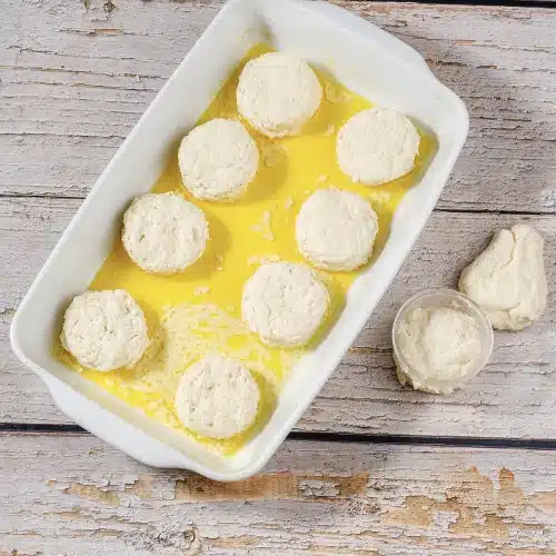 Nine cut rounds sitting in melted butter in a white baking dish