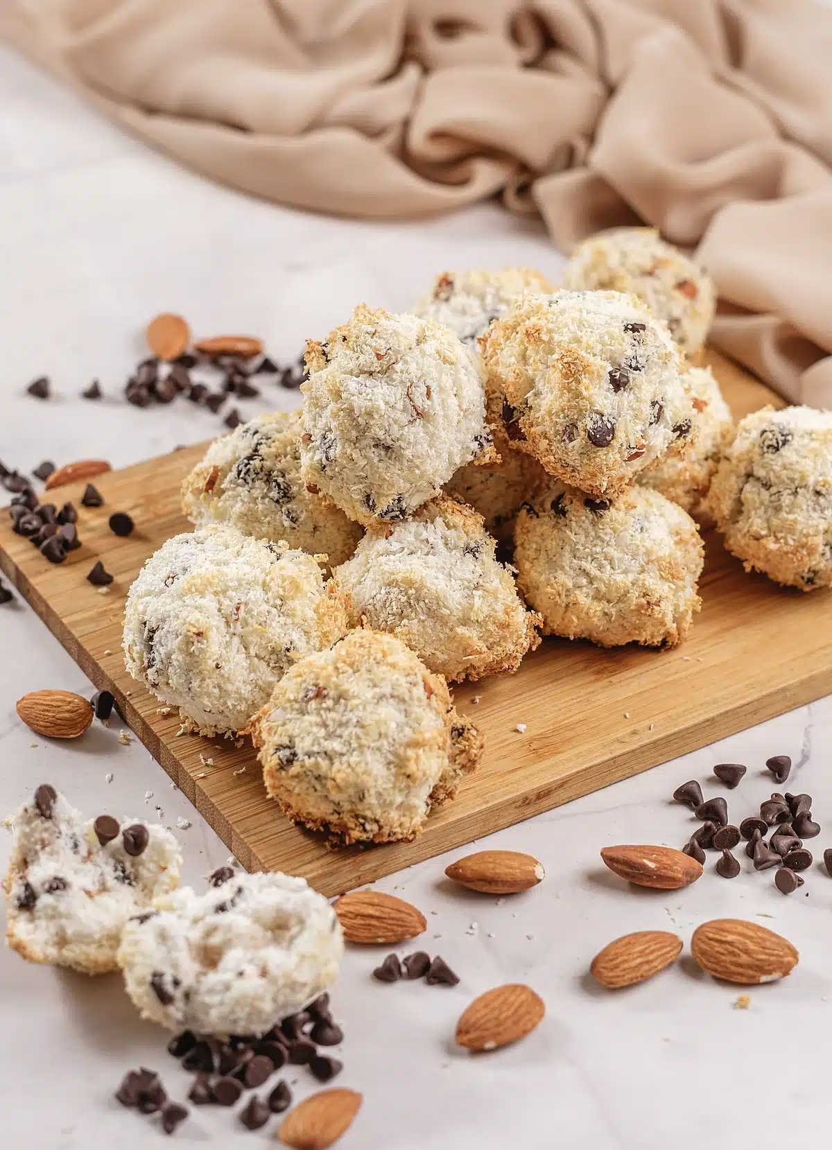 Almond Joy cookies piled high on a bamboo board with nuts scattered around