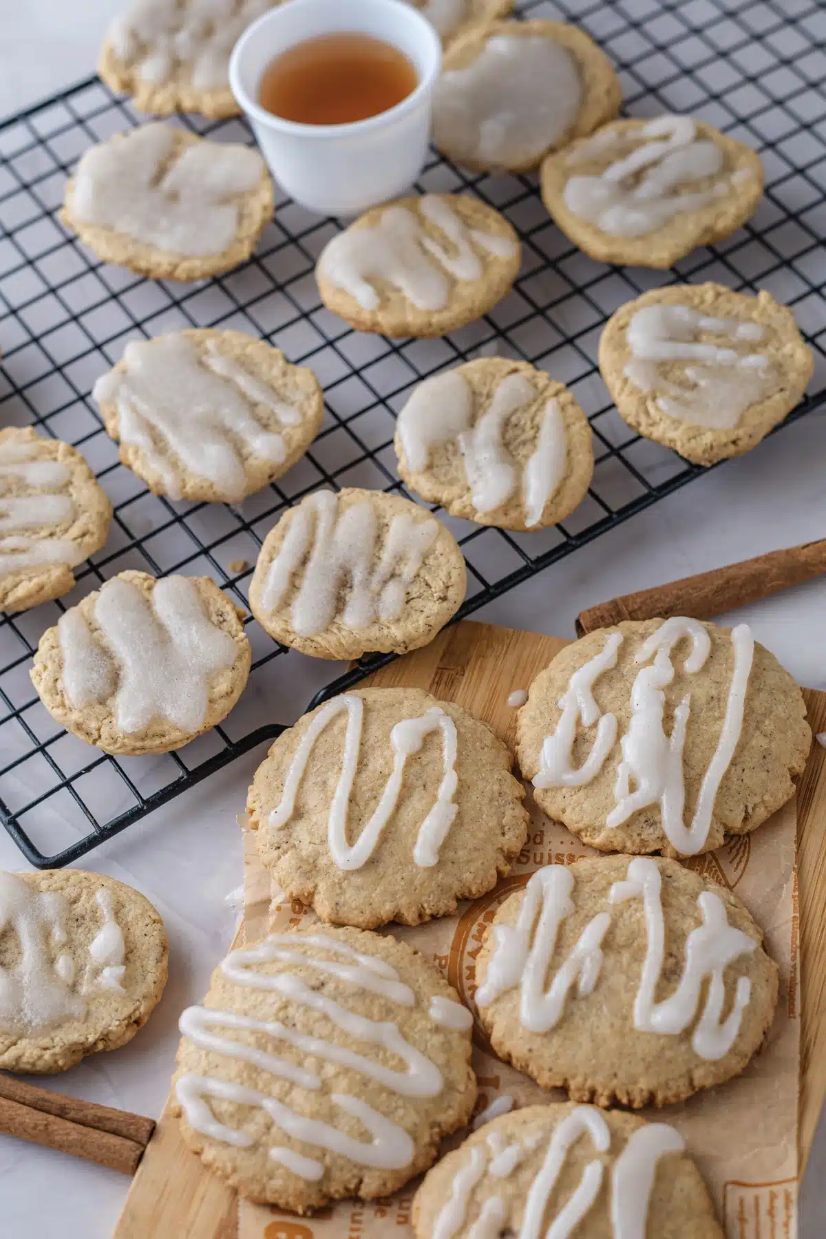 Apple cider cookies with piped zigzag glaze on a wooden board, seen from an angle, with more cooling on a rack behind