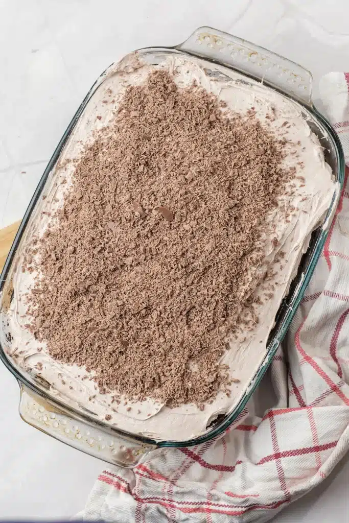 Baileys poke cake in a glass dish seen from directly above, the whipped topping covered in grated chocolate