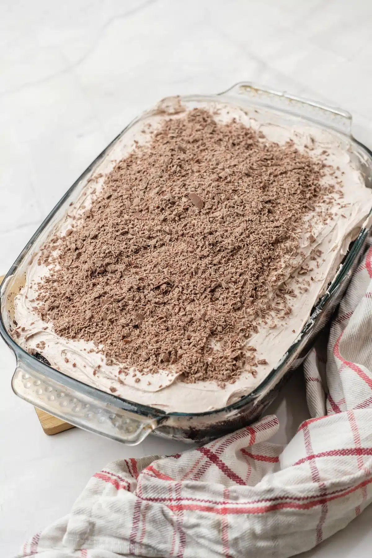 Baileys poke cake in a glass baking dish, the whipped topping covered in grated chocolate, on a red-striped cloth