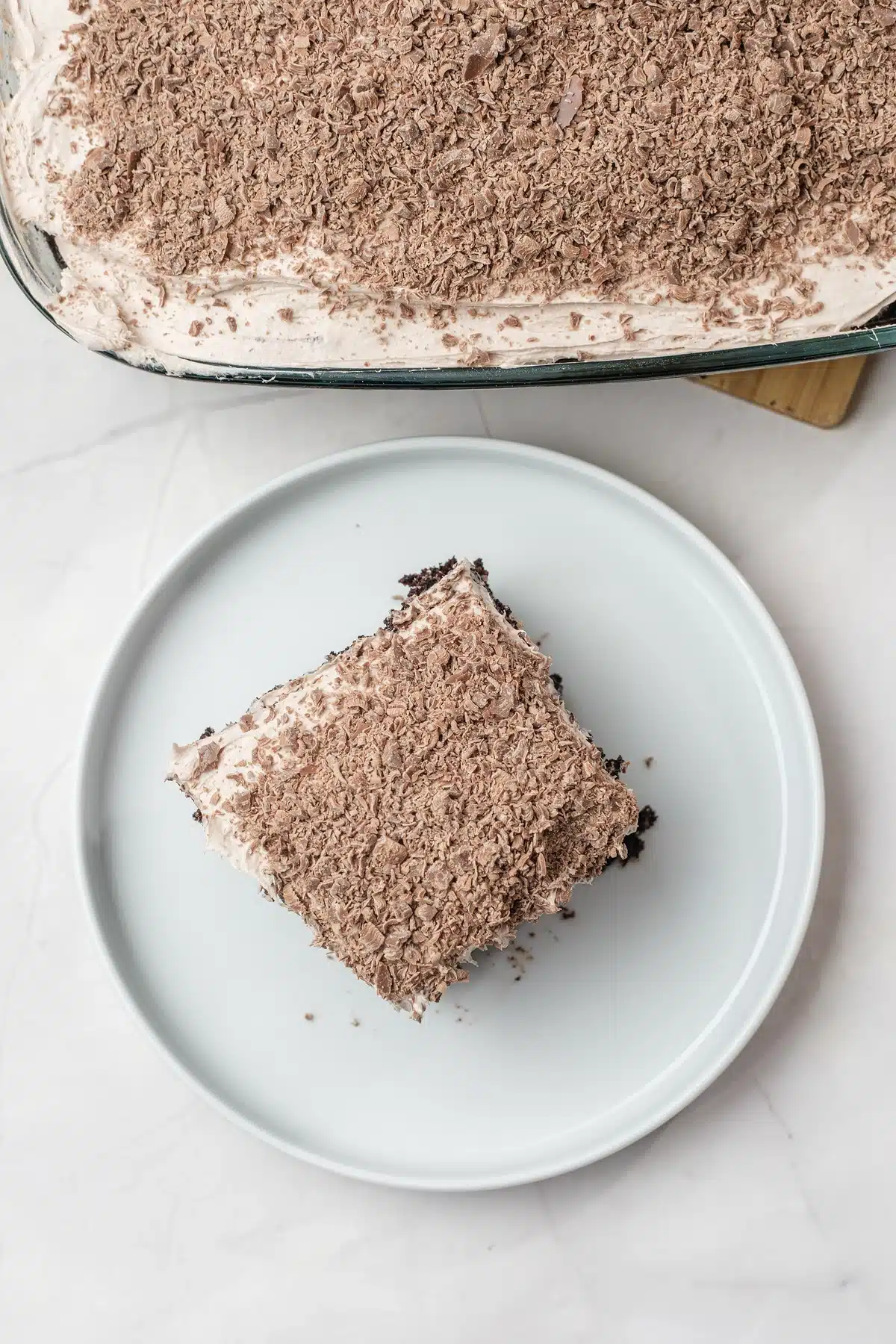 A square of Baileys poke cake on a white plate seen from above, the topping covered in grated chocolate