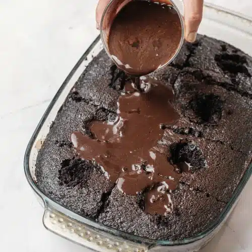 The chocolate filling poured from a bowl over the poked cake