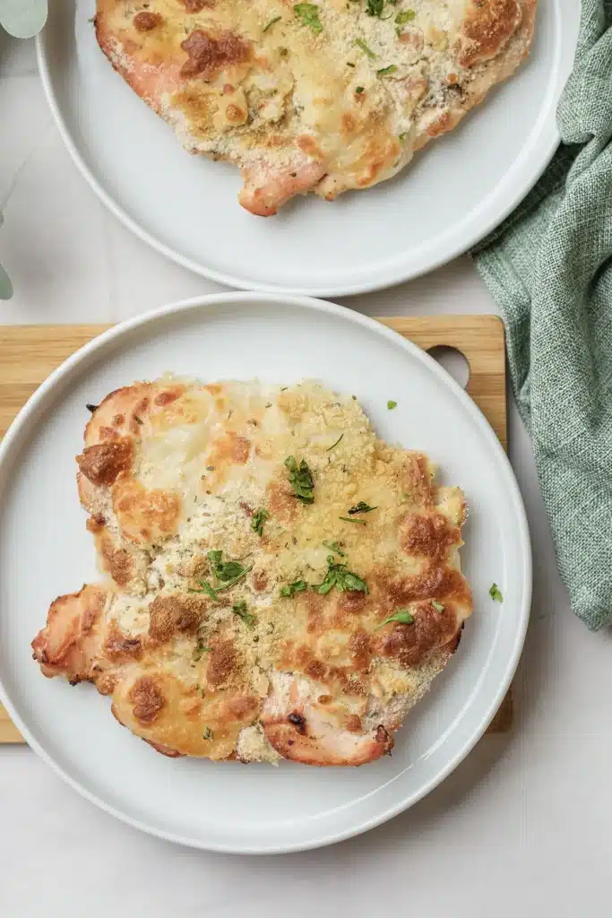 Baked Caesar chicken on a white plate, seen from directly above, with a golden cheese top and chopped parsley