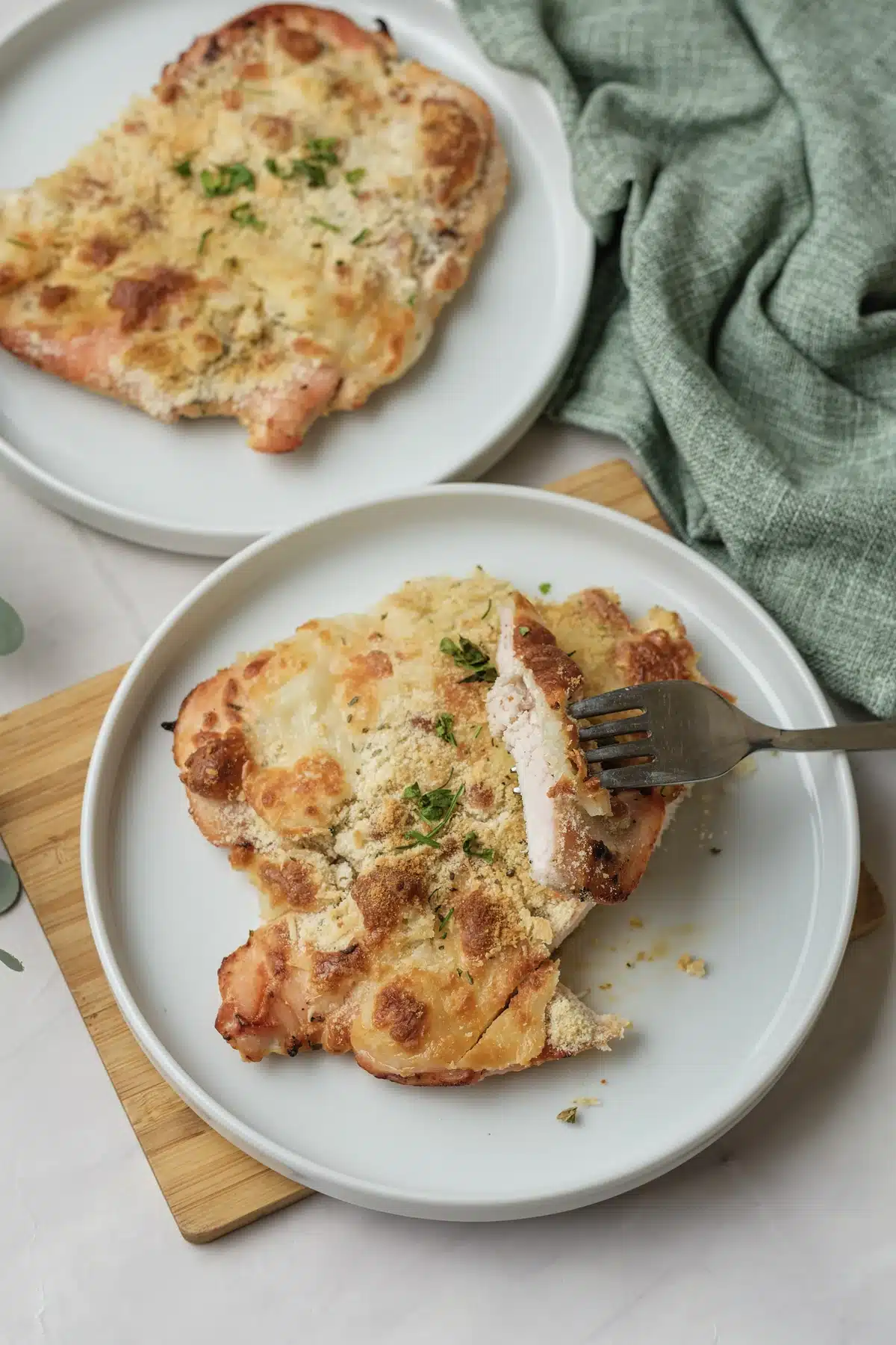 A fork holding a cut piece of the breast, showing white, juicy meat under the golden topping