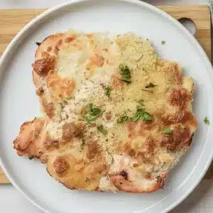 A single plate of Caesar chicken with a golden cheese and breadcrumb top and parsley
