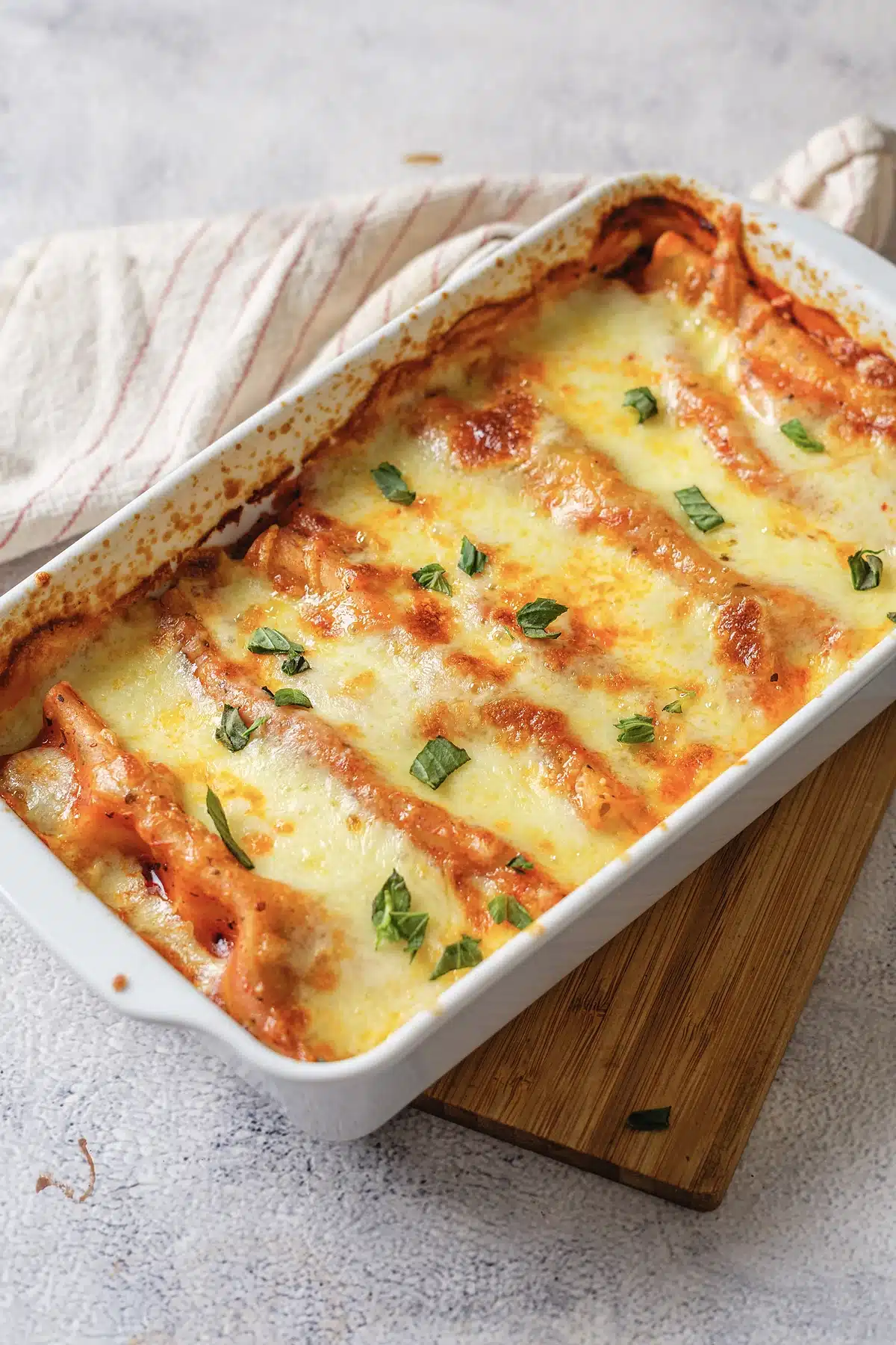 Baked manicotti bubbling in a white dish on a wooden board
