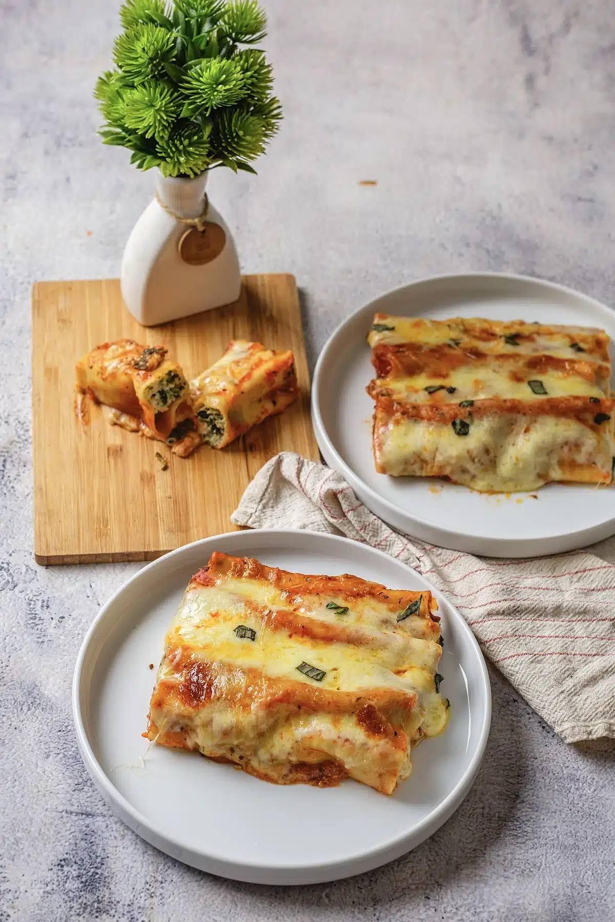 Baked manicotti plated beside a board of tubes cut open to show the filling
