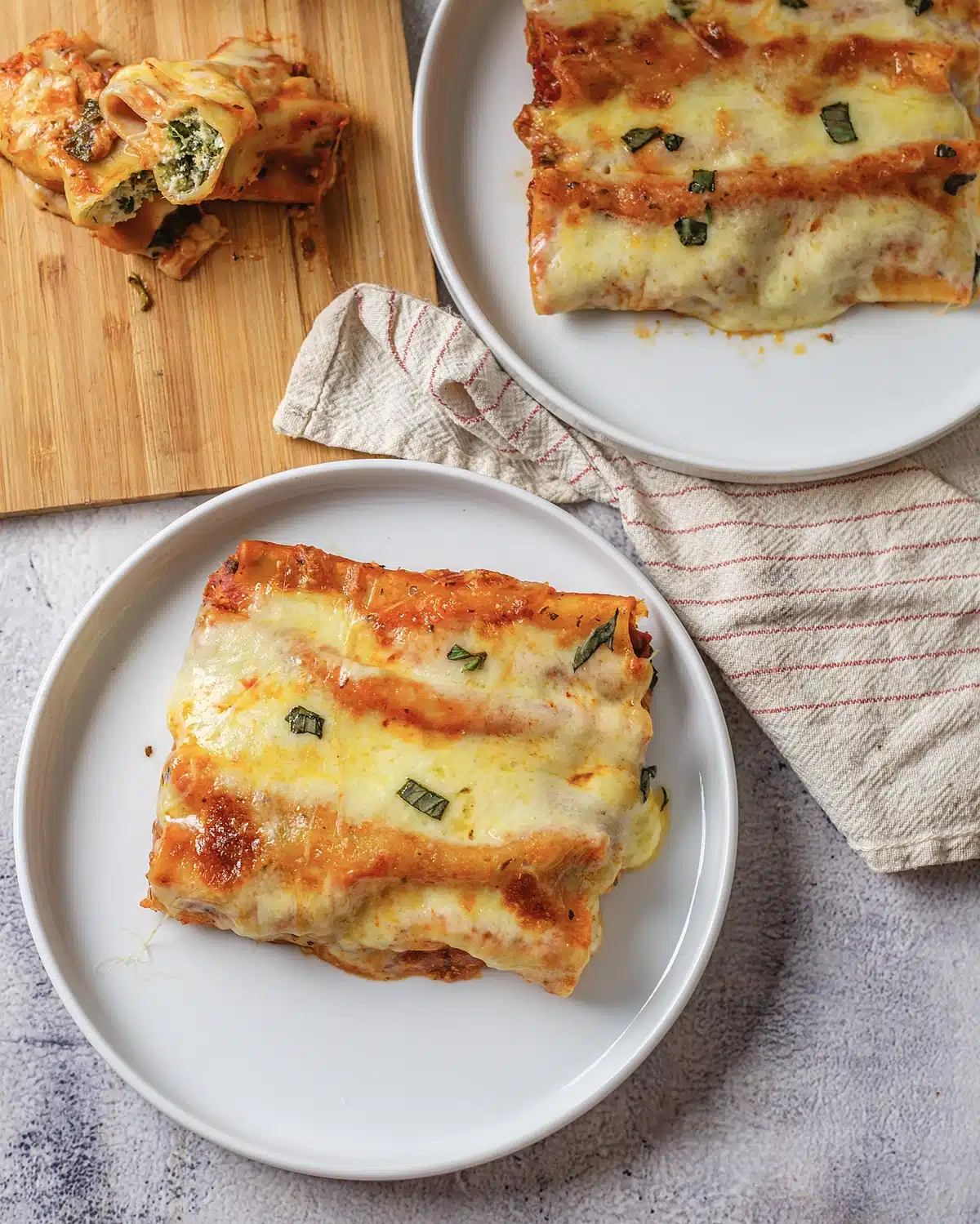 Baked manicotti on a white plate with a striped towel behind