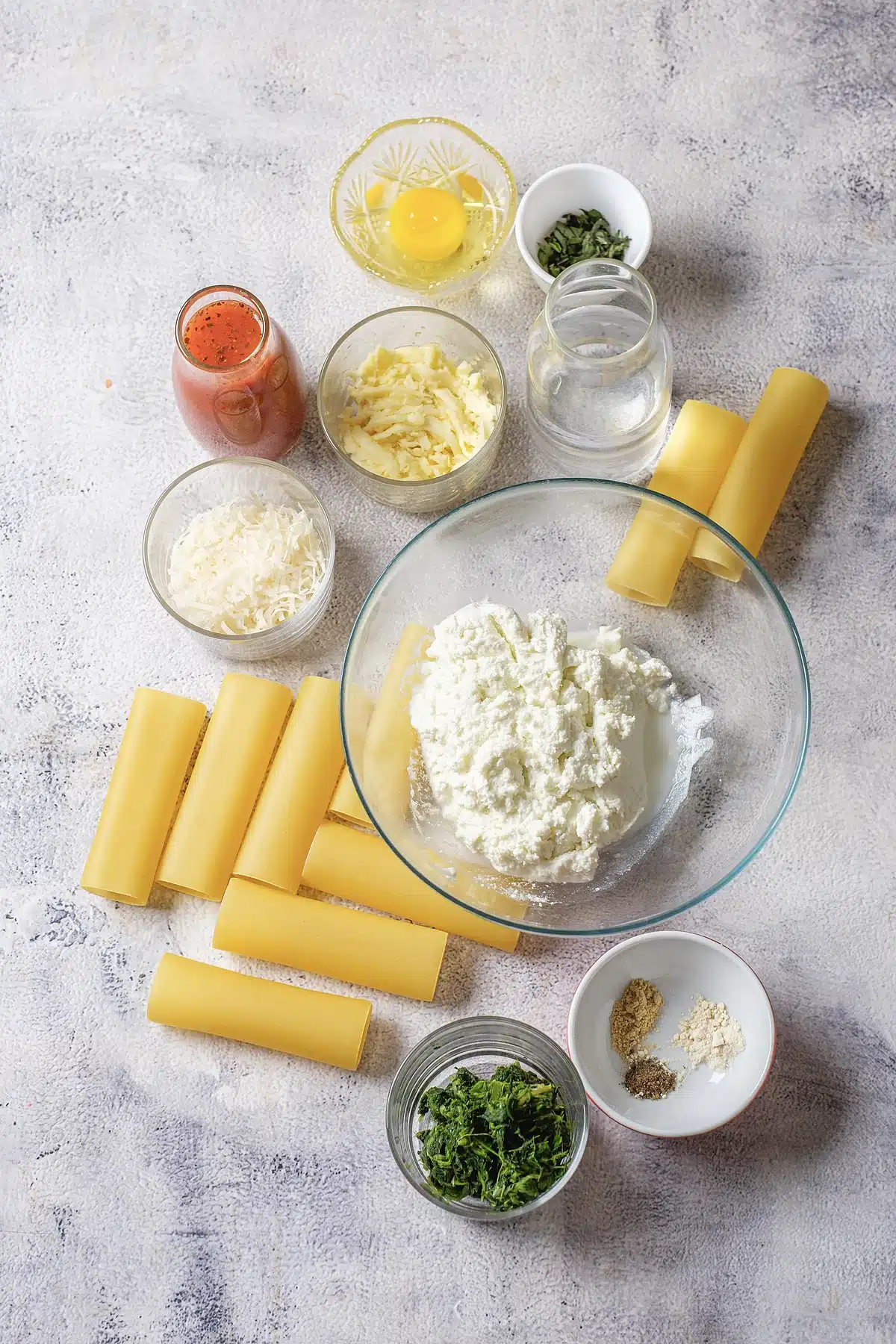 Manicotti shells, ricotta, mozzarella, parmesan, egg and marinara laid out on a counter