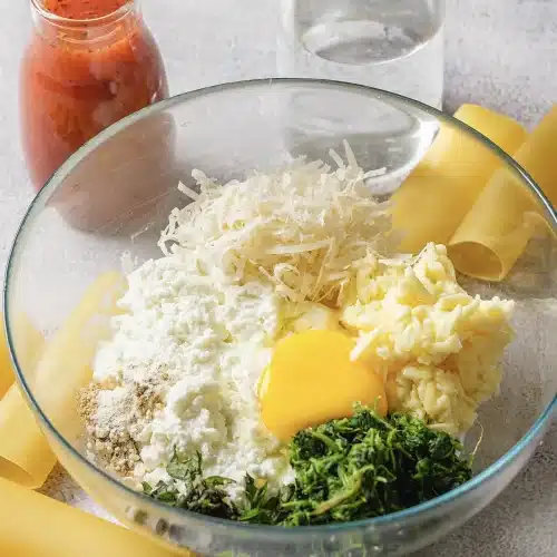 A close glass bowl of ricotta, mozzarella, parmesan, egg yolk and chopped greens
