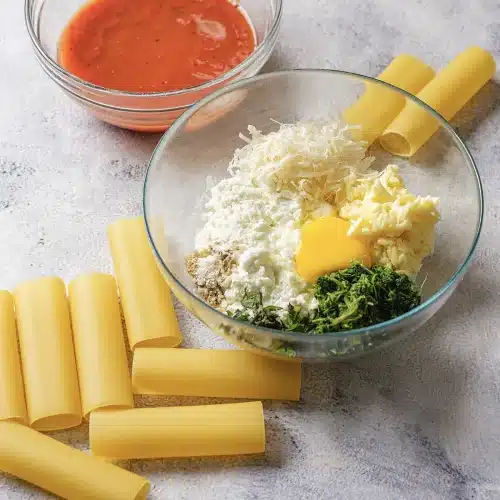 A glass bowl of thinned tomato sauce beside the bowl of cheese filling