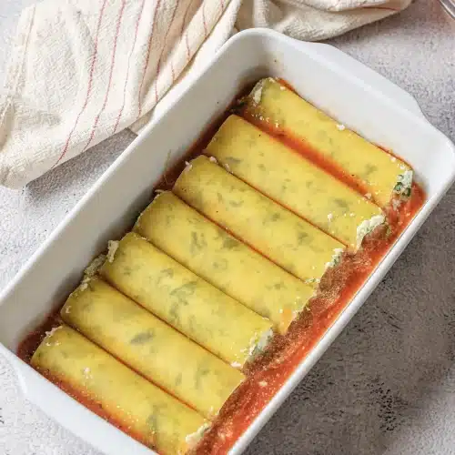 Filled tubes laid in a single layer over sauce in a white dish