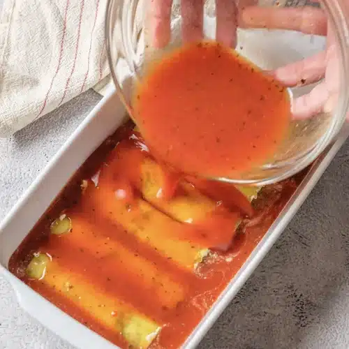 Thinned tomato sauce poured from a glass bowl over the filled tubes