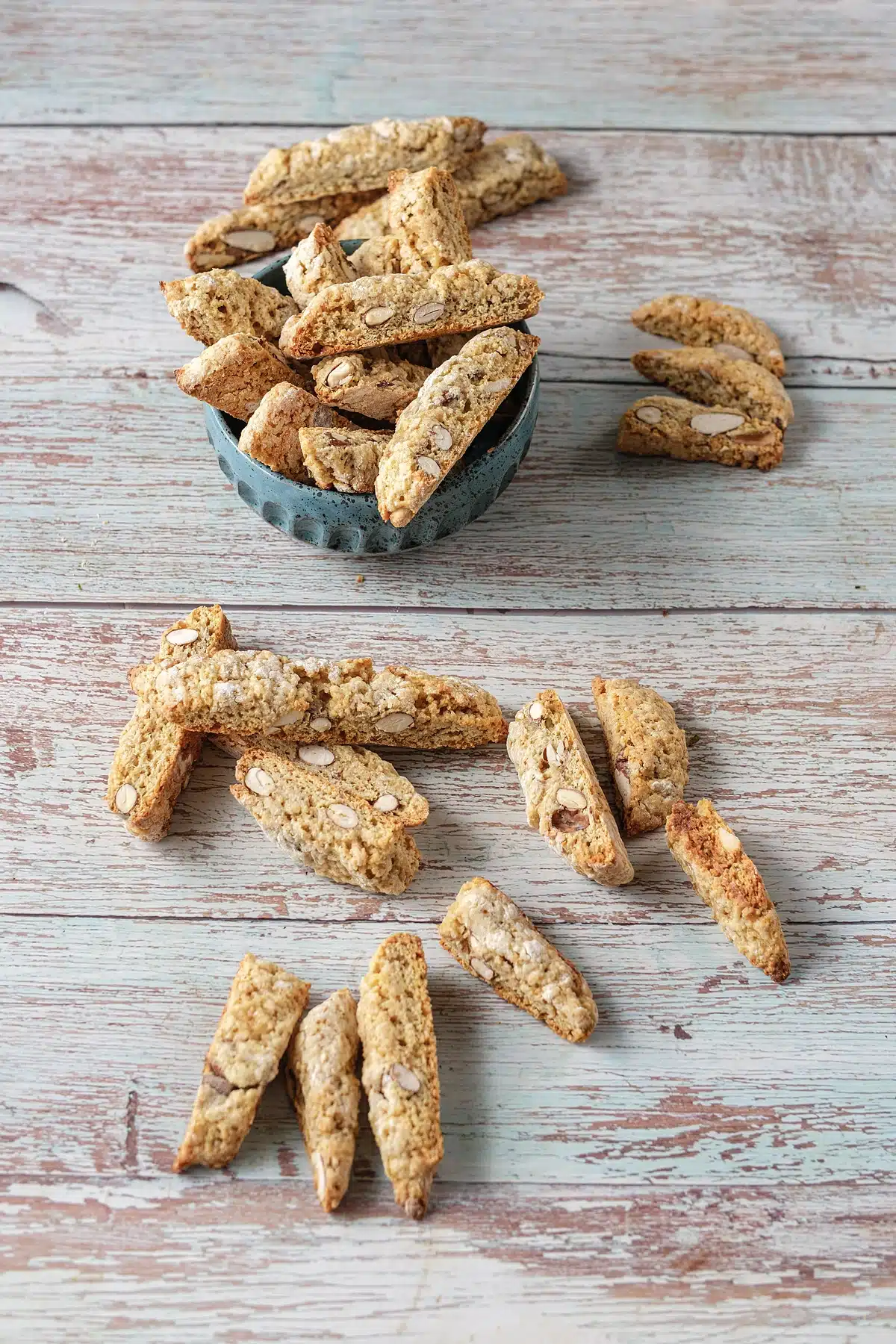 Overhead view of almond biscotti in a small blue dish with slices scattered around