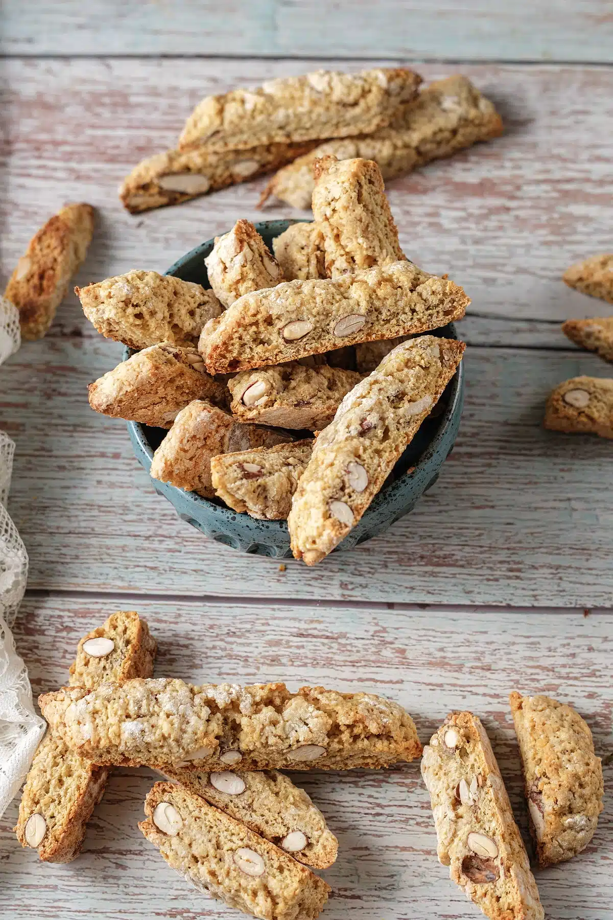 Almond biscotti heaped in a blue bowl with more slices on the table