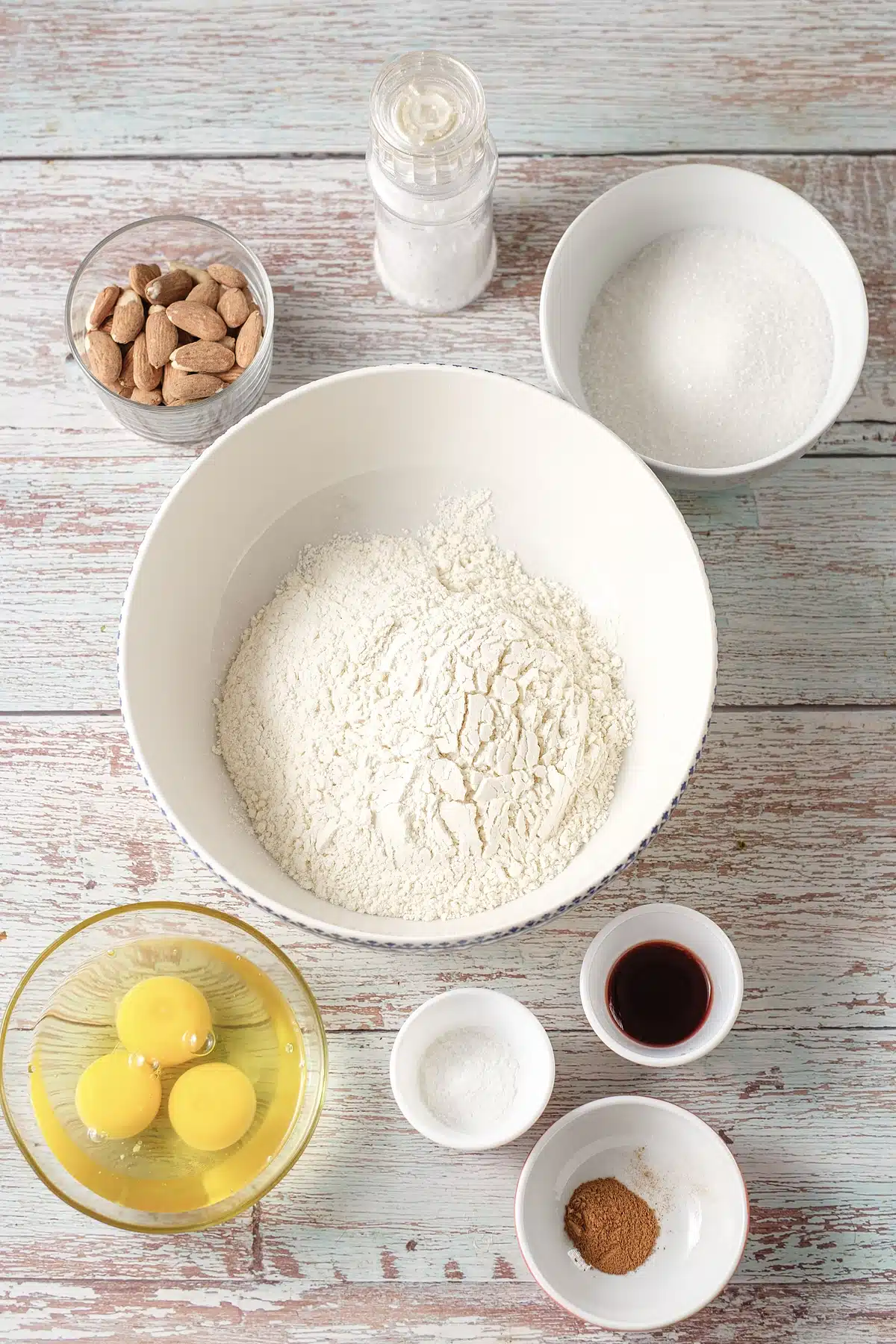 Flour, sugar, eggs, vanilla, nutmeg and whole nuts in bowls on painted wood
