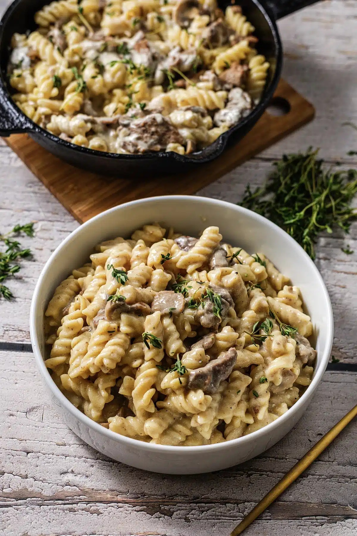 Beef stroganoff served in a white bowl with the skillet behind on a board