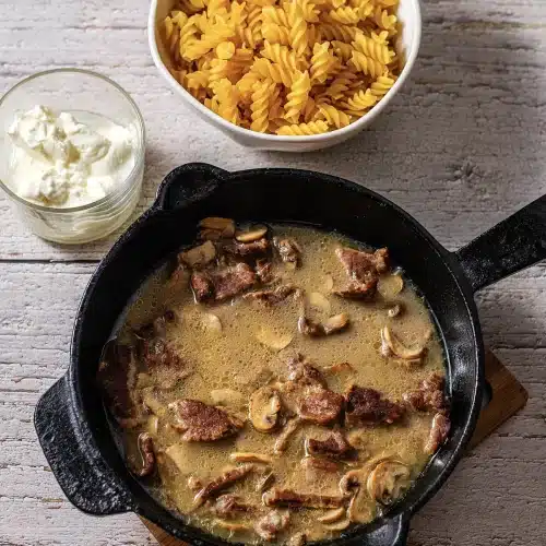 Seared strips of meat and sliced mushrooms simmering in broth