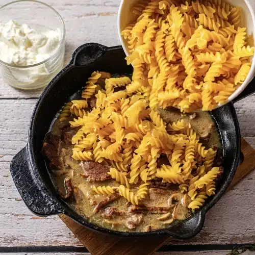 Dry twisted pasta tipped from a bowl into the simmering skillet