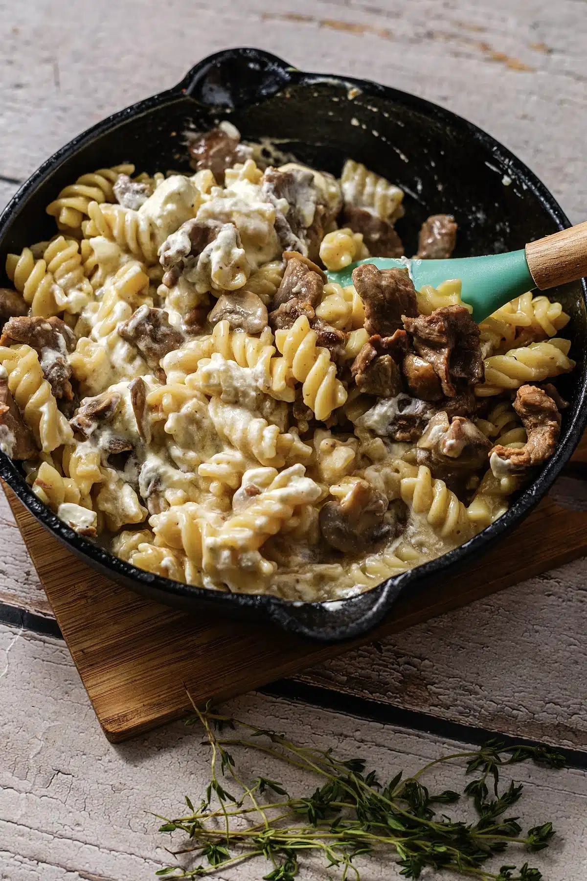 A wooden spatula turning creamy pasta and browned meat through a black skillet