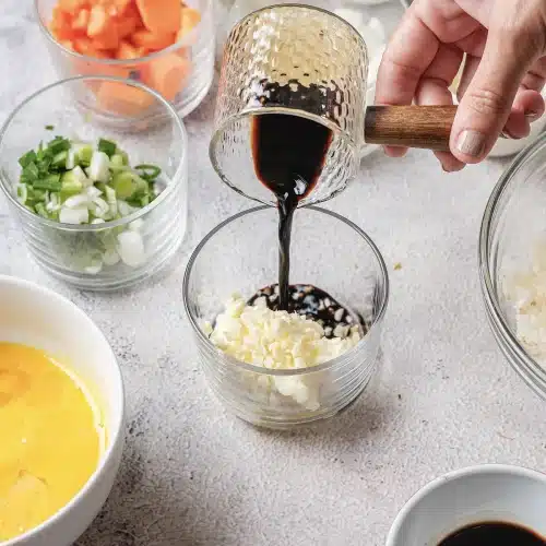 Dark soy sauce poured from a copper pitcher into the garlic and butter