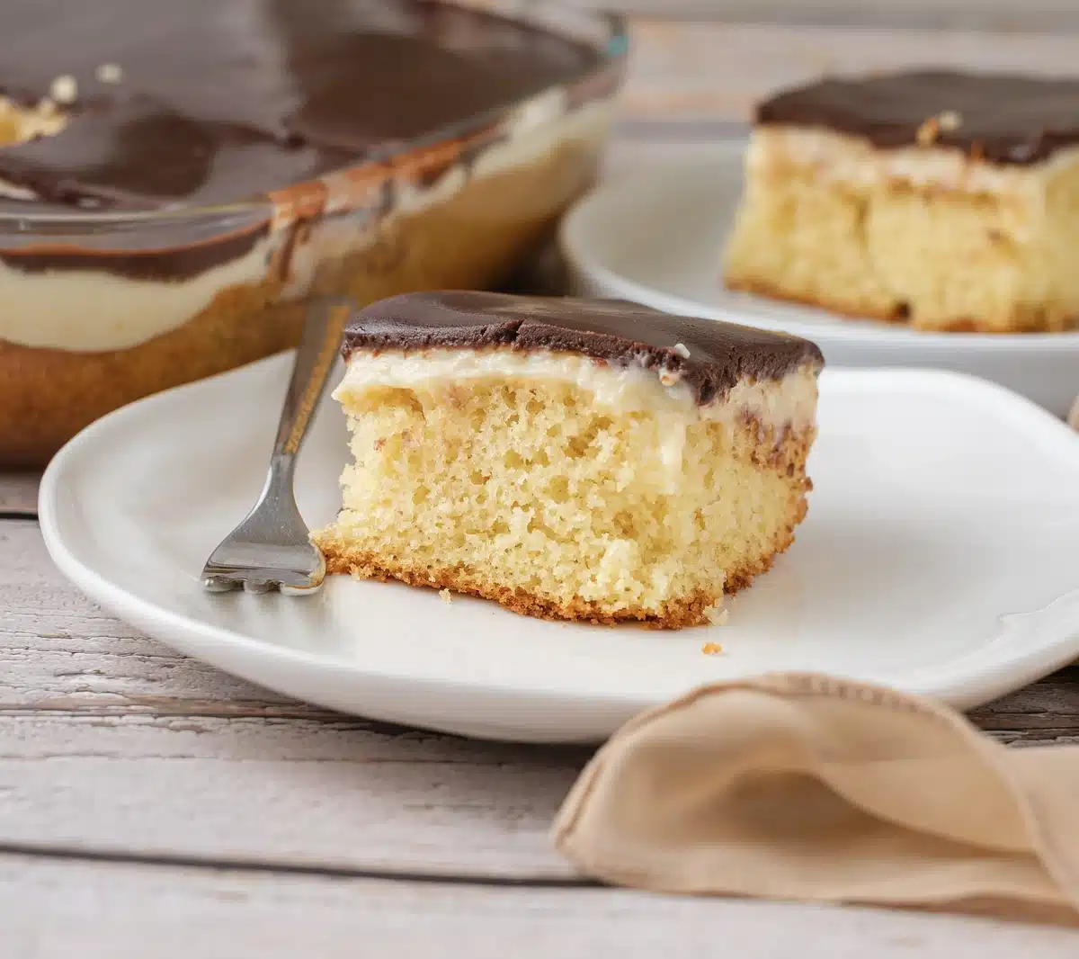 A cut square on a white plate with a fork, showing the pudding-soaked yellow layer under the dark chocolate