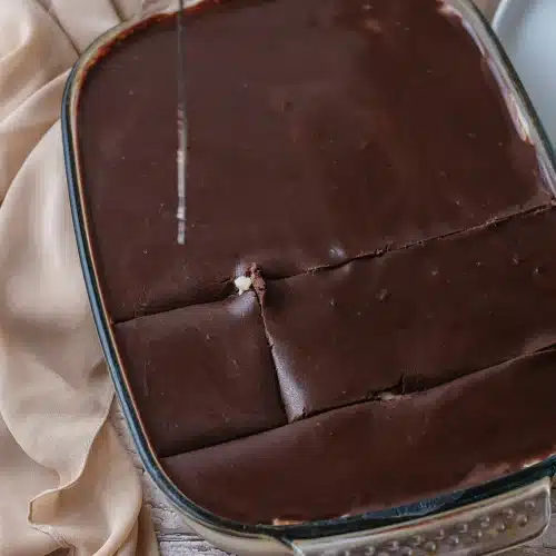 A knife cutting the set ganache top into squares in the glass dish