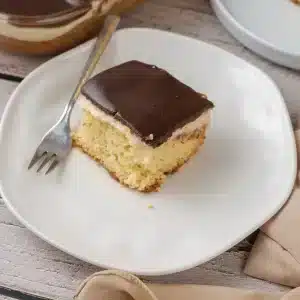 A single square of Boston cream poke cake on a white plate with a fork