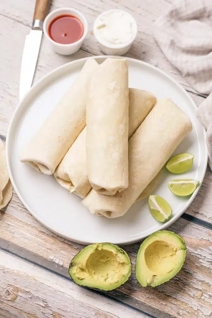 Breakfast burritos stacked on a white plate seen from directly above, with lime wedges and avocado halves beside