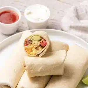 A single breakfast burrito cut in half on top of the stack to show the filling
