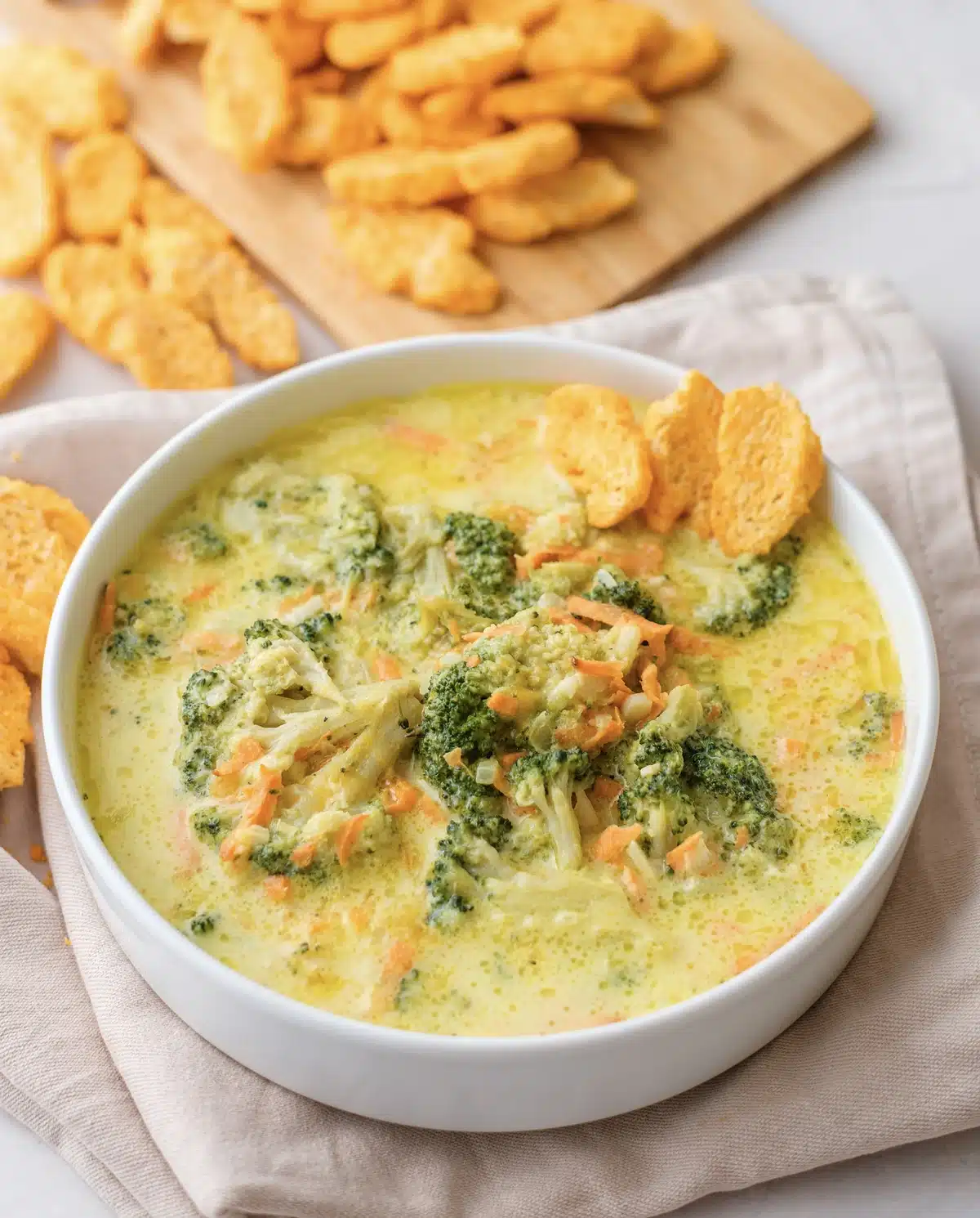 Broccoli cheddar soup seen from above, thick and yellow with whole florets and a board of cheese crackers behind