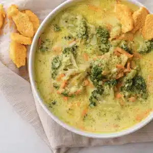 A single bowl of broccoli cheddar soup with whole florets and cheese crackers on top
