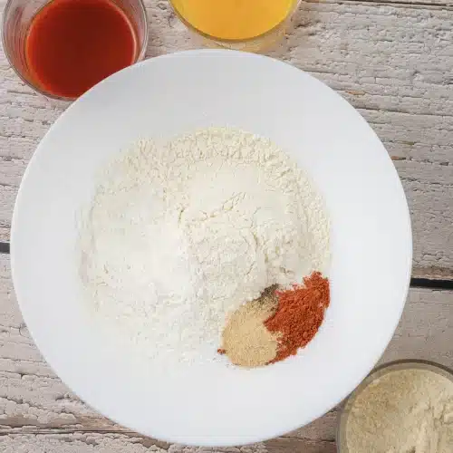 Flour in a white bowl with paprika, garlic powder, onion powder and salt on top
