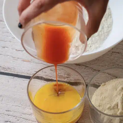 Hot sauce poured from a glass into a glass of beaten egg
