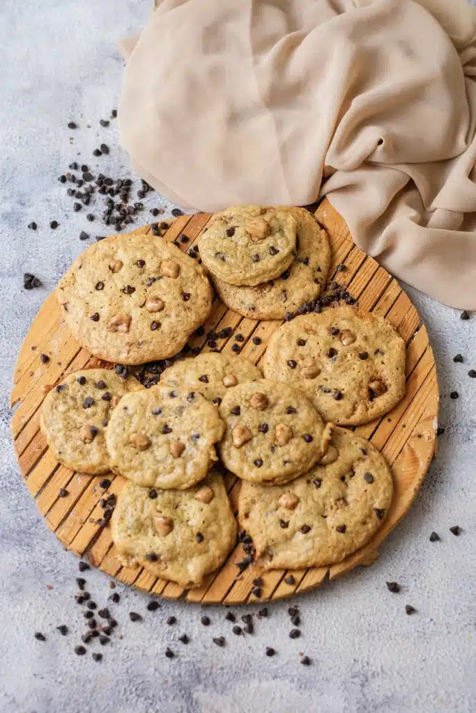 Butterscotch chocolate chip cookies on a round wooden rack with a beige cloth, seen from directly above
