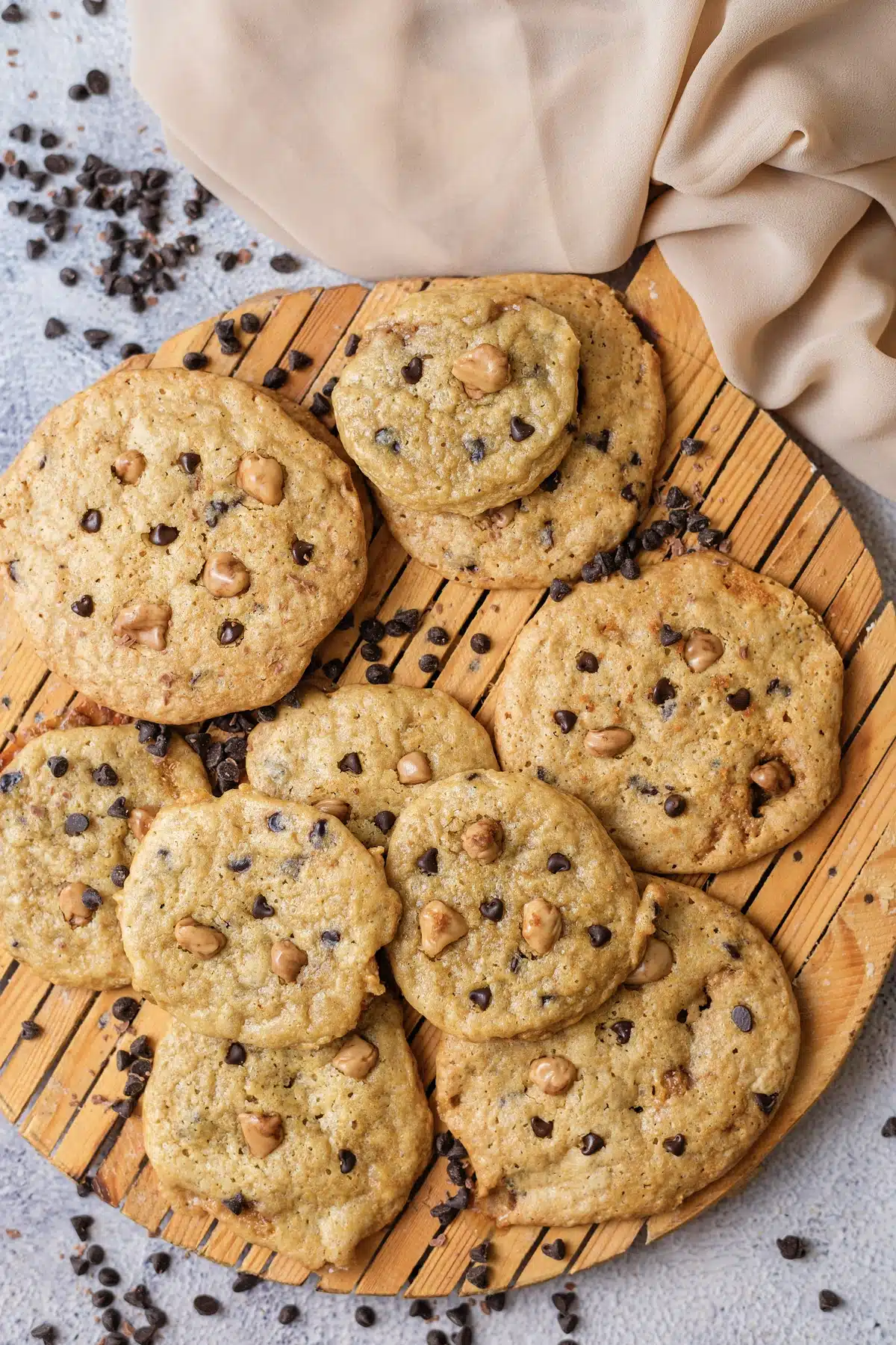 Butterscotch chocolate chip cookies piled on a round wooden board, seen from directly above