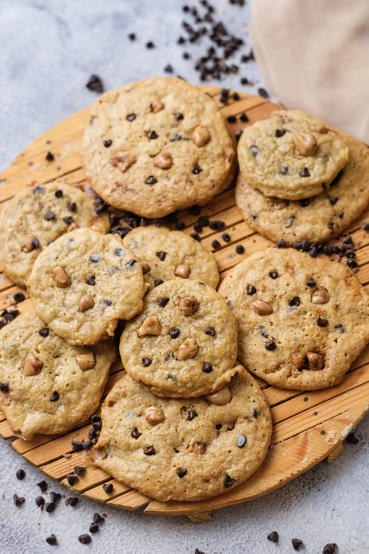 Butterscotch chocolate chip cookies on a wooden board with scattered chips and a beige cloth behind
