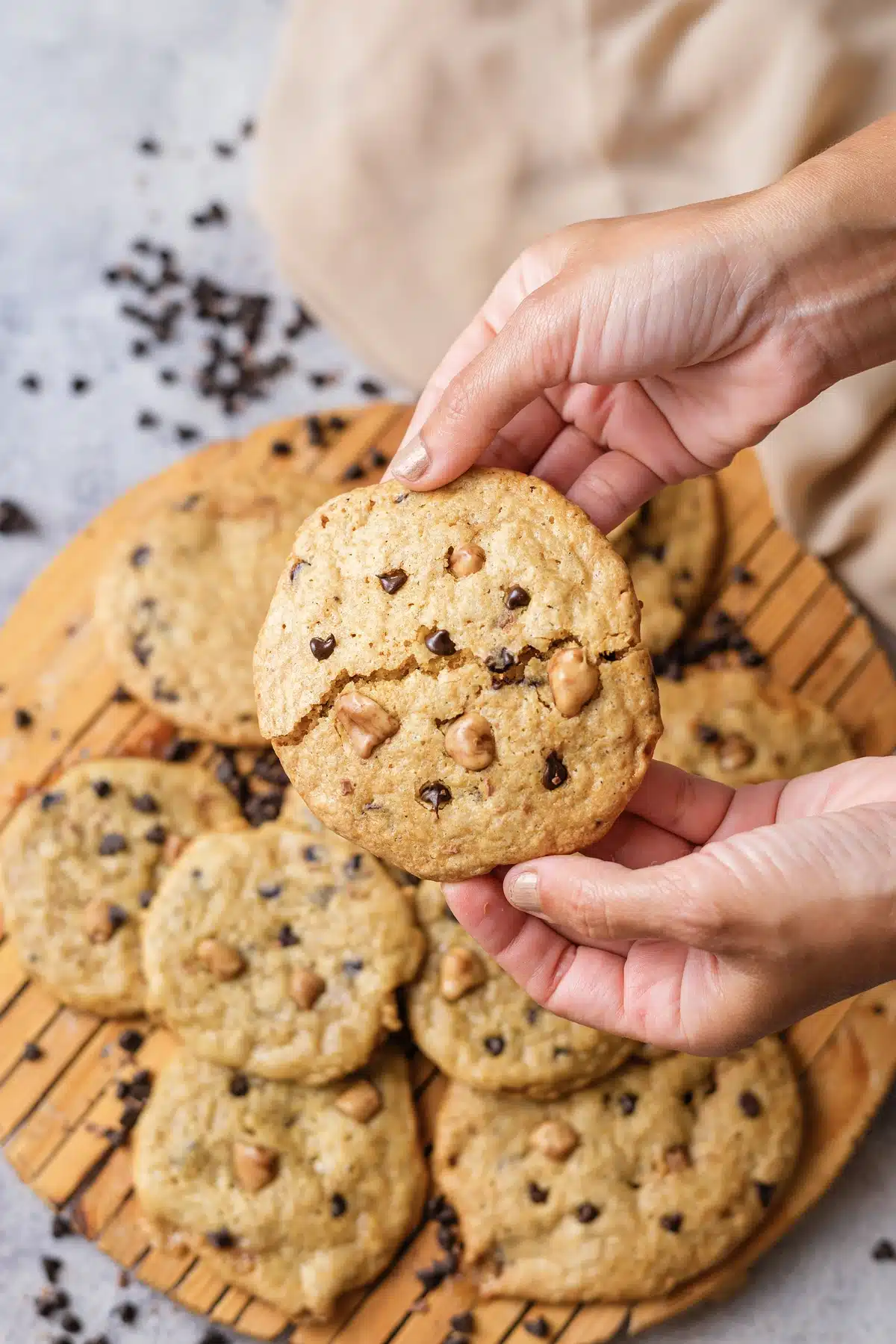 Two hands holding up one cookie with a crack across it above the rest on the board