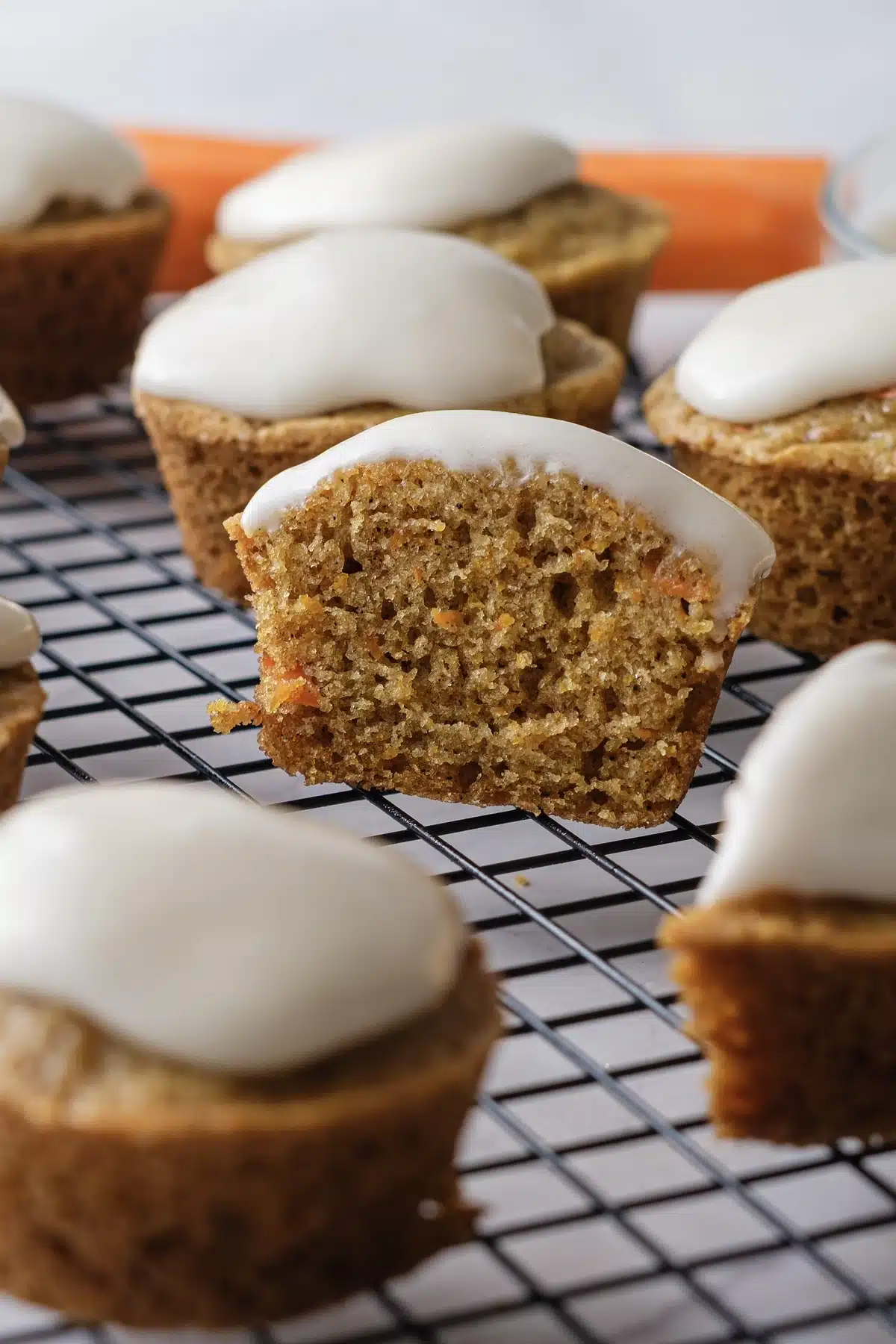 A carrot cake cupcake cut in half to show the moist, orange-flecked crumb under the frosting