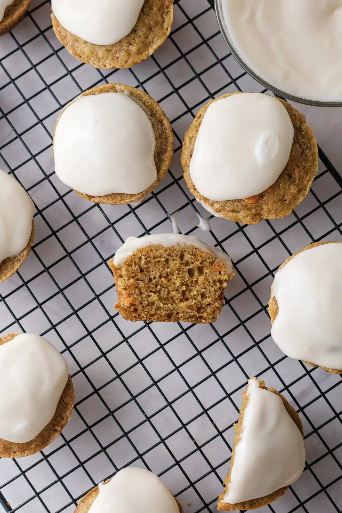 Carrot cake cupcakes from above on a wire rack with one cut open beside a bowl of frosting