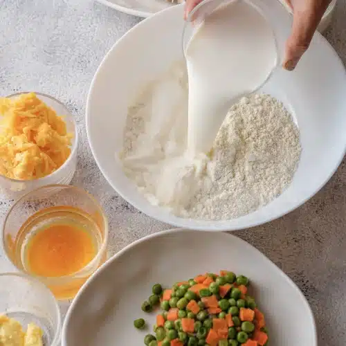 Milk being added to the dry biscuit mix in a white bowl