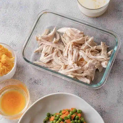 Shredded chicken spread over the bottom of a glass baking dish