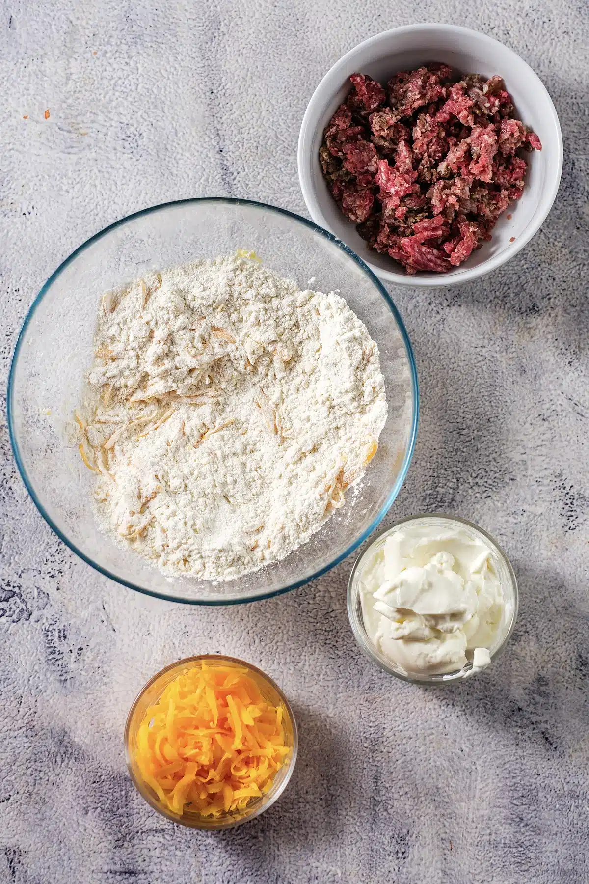 Ground pork, dry biscuit mix, grated cheese and cream cheese in glass bowls