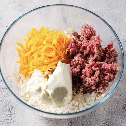 Dry biscuit mix, grated cheese, cream cheese and raw pork together in one glass bowl