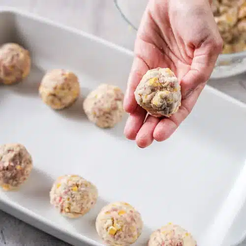 A hand rolling the mixture into a ball above a lined white tray