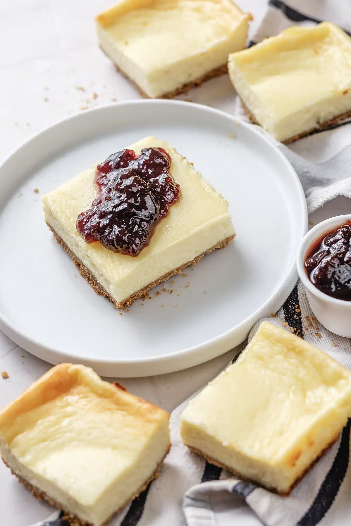 Cherry cheesecake bars with one square plated and two more on a striped cloth