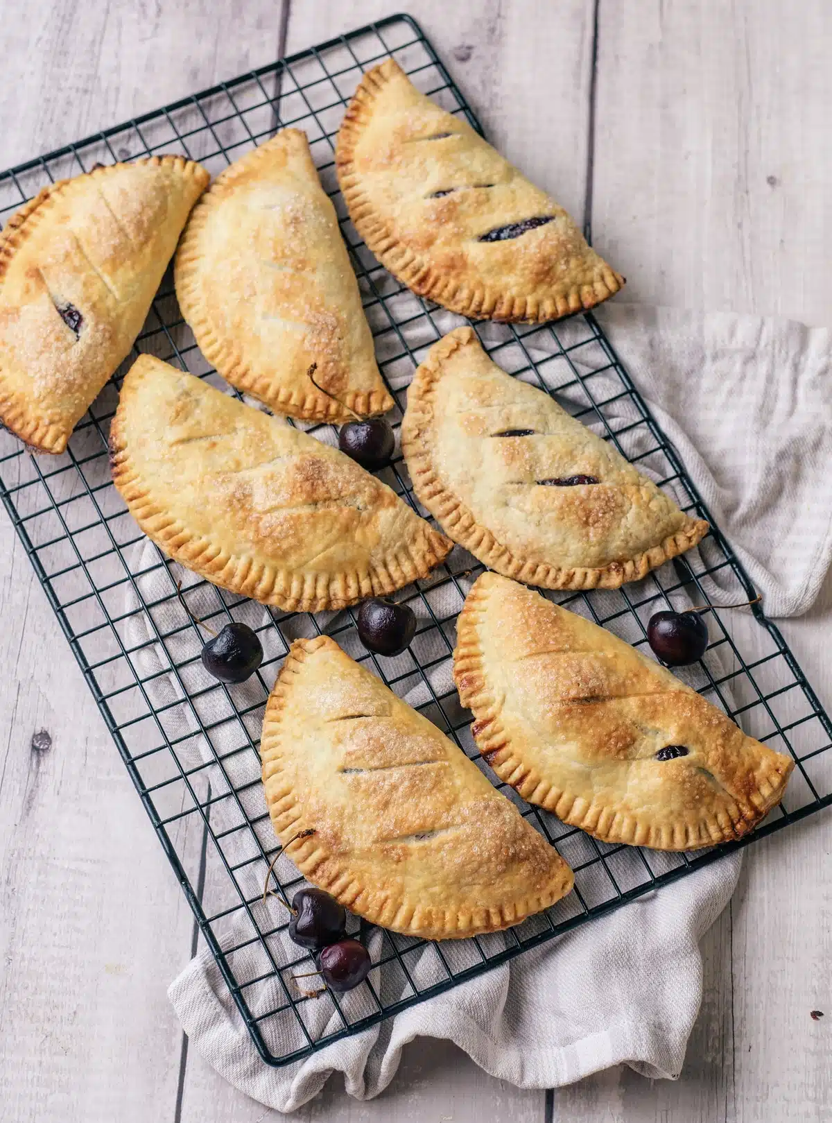 Cherry hand pies cooling on a black wire rack with fresh cherries scattered between them